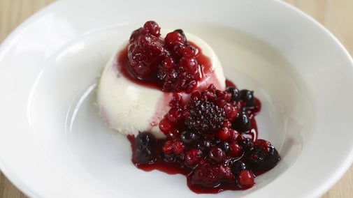 A mound of creamy white panna cotta in a white bowl, with berry compote on top